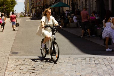 Madrid, İspanya. 1 Haziran 2022. Orta yaşlı bir kadın bir yaz günü eski bir Avrupa caddesinde bisiklet sürüyor. Aktif şehir hayatı, günlük eğlence. Dışarıya gidip gelen insanların tam boy görüntüsü.. 