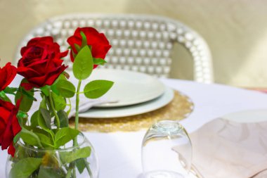 Randevu masası Pahalı bir restoranda güzel bir masa. Vazodaki kırmızı güller masa örtüsünü süsler. Tabaklar, bardaklar masanın üstünde. Düğün kutlaması. Kafe terasında klasik servis.