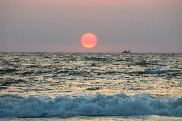 A huge orange and yellow sun over the sea, the ocean at sunset. The sun is setting over a horizon. Unquiet water with waves rolling on a shore. A seascape without people. Calm evening, twilight scene.