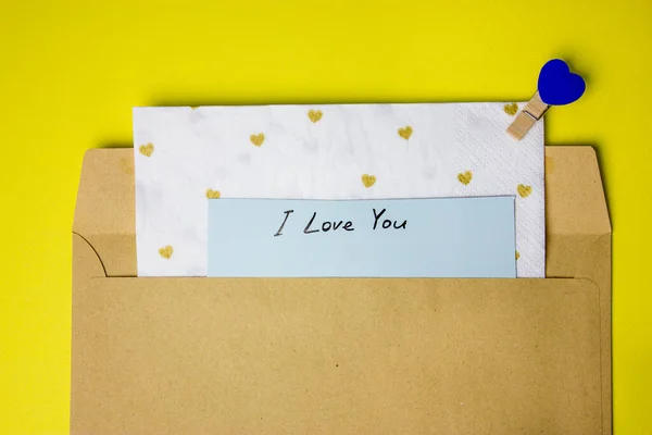Cardboard envelope with note with the text of a declaration of love on a yellow background flatly. Present for Valentine\'s Day. A letter for the beloved ones. I LOVE YOU handwritten text. Small hearts