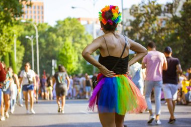 Madrid, İspanya. 25 Temmuz 2022 'de bir sürü insan Onur Ayı' nda toplandı. Gökkuşağı etekli şık bir kadın, şehir caddesinde gey geçit töreninde duruyor. Yaz seyahati, eğlence, dışarıda eğlence.