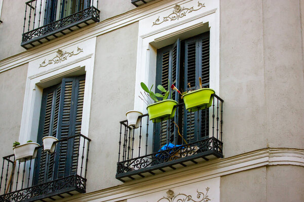Madrid, Spain. May 3, 2022 Stucco facade of white residential house, building with balconies, windows with wooden shutters. European city street architecture. Real estate. Balcony garden, green plants