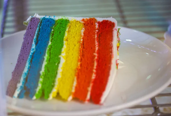 Delicious rainbow cake cut with colored filling, layered colored cakes. Sweet dessert on a white plate. Pride month concept, gay symbol. Striped slice of a prepared rainbow bakery. Baked layer cake.