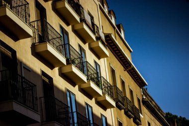 The facade of an old apartment building with contrasting shadows against a blue sky. Urban European architecture of Spain, Madrid. Yellow house with many balconies against blue sky. Travel destination