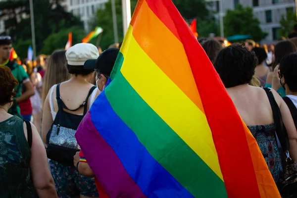 A brightly colored rainbow flag in the hand of an activist at the Pride month march. Lots of people, crowd at gay pride parade in Madrid, Spain in summer 2022. Faceless human. Sexual minorities. 