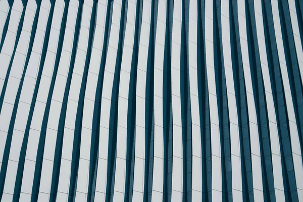 Lines in architecture. Modern office facade. Fragment of tall blue building with contrast shadows. Abstract built structure background. Business quarter in a modern city. Urban scene pattern, texture.