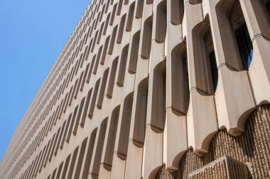 Modern architecture in the style of brutalism. Fragment of a concrete building looking up from below into perspective against a blue sky. New Brutalism is a branch of postwar architectural modernism. 