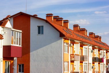 Mavi gökyüzüne karşı terra cotta kiremit çatı kiremitleri olan yenilenmiş beyaz apartman önü. Yeni inşa edilmiş, bacaları, küçük pencereleri, kil çatıları olan modern bir ev. Emlak yatırımı