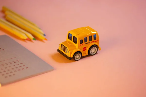 Toy yellow American school bus on table, calendar with dates, colorful wooden pencils lying on pink table. Stationery for studying, drawing, planning. Back to school in September. Supplies for study.