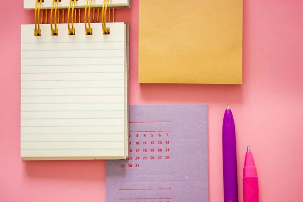 Nice composition of stationery, tools for studying in school, university, work. Calendar, planning notebook, ballpoint pens lie on pink table flatly top view. Back to school concept. Female business.