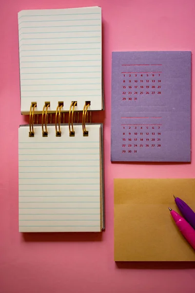 Composition of stationery, tools for studying in school, university, work. Calendar, planning notebook, ballpoint pens lie on pink table flatly top view. Back to school concept. Female business.