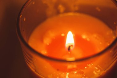 A pink or red wax scented candle in a glass container with a burning flame. Items to make the home cozy. Spa, relaxation. Memory, passion, love concept. Selective focus. Valentine's Day holiday.