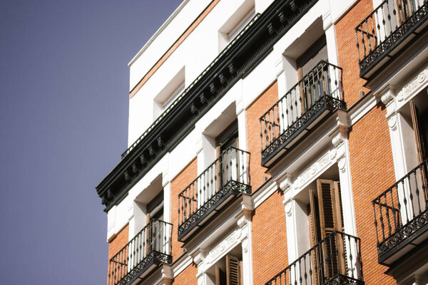 Madrid, Spain. August 1, 2022 Facade of a beautiful vintage red brick building with black balconies. Corner of an apartment house against a blue sky. Neoclassical architectural style in a Spanish city