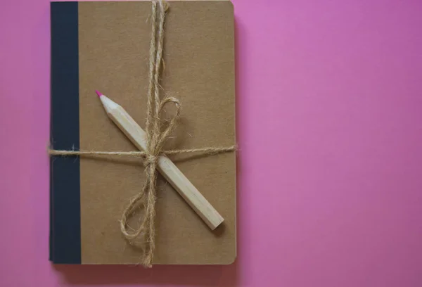 Record journal tied with burlap rope with bow on pink background with space for text top view. Pink wooden colored pencil for drawing, notes flatly. Female secrets concept. Back to school concept.