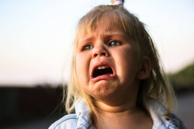 An unhappy sad child crying profusely close-up portrait. An ugly grimace. Abandoned child lost in the street. Negative emotions, disappointment, pain, sadness, unhappiness concept. Tears in kids eyes.