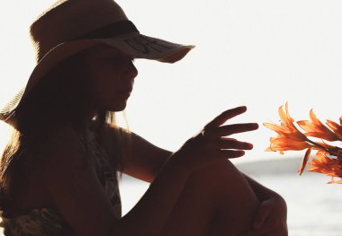 Little girl in hat touch lily buds petals with hand. Dark enigmatic silhouette of a teenage child portrait in profile at sunset on seaside, river coast in summertime. Summer holidays. Floral postcard.