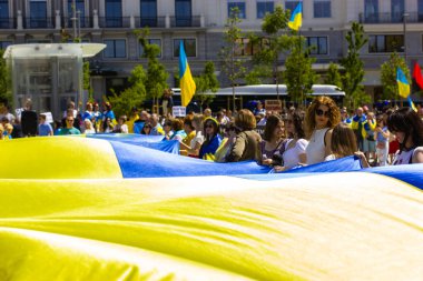 Madrid, Spain. July 1, 2022 A crowd of patriots at rally in support of Ukrainians in Russia's war. People are holding a huge yellow blue Ukrainian flag, a symbol of Ukraine's independence. Save Ukraine