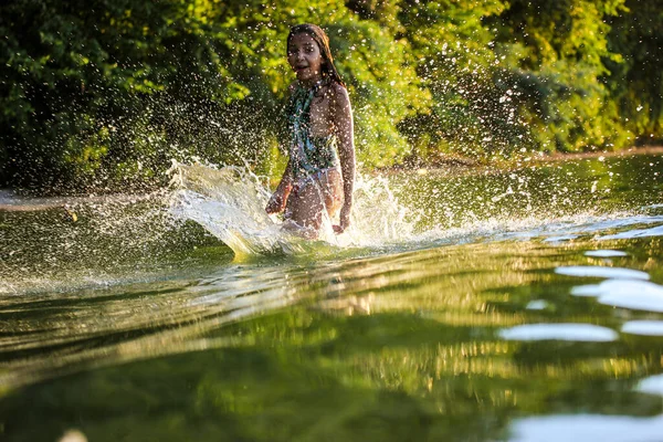 A teenage girl splashing in green water of a river, lake in summer day. Summer vacation fun, joy. Female child 10-12 years at a children\'s camp. Fun, joy, excitement. Green wave, splashing water.