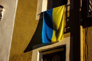 Yellow-blue flag of Ukraine outside window of a residential building as a sign of support for Ukrainians in connection with Russia's military aggression. War in Ukraine concept. Symbol of independence