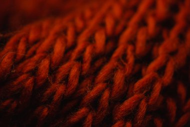 Siyah arka planda sıcak kırmızı örgü eşarp. Yün ürünün dokusu, soğuk mevsim için bir aksesuar. Kıyafet, ekose kumaş, el yapımı iplik battaniyesi. Örgü ve dikiş işi. Rahat yün moda..