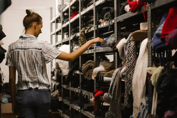 Madrid, Spain. September 1, 2022 Young woman walks among rows of shelves of shabby clothes. A girl picks out clothes at a refugee shelter, second hand. Humanitarian aid help to the homeless, destitute