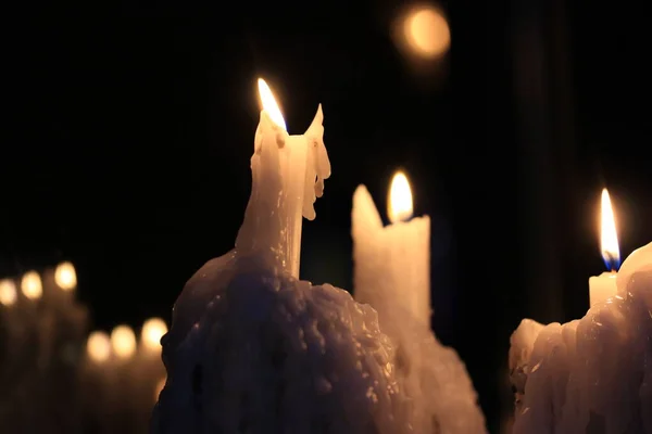 A lot of white wax candles with burning lights on a black background. Romantic atmosphere. Burning candles in church. Warm flame lightning. A symbol of faith, religion, hope. Lighting a room at night.