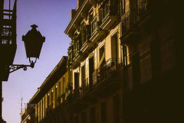 Eski bir Avrupa caddesinin güzel fotoğrafı, evler cepheler, balkonlar, akşam gökyüzüne karşı Victoria tarzı klasik fener. Bir seyahatten kartpostal, İspanya, Madrid 'e seyahat. Kasabada günbatımı. Alacakaranlık şehri.