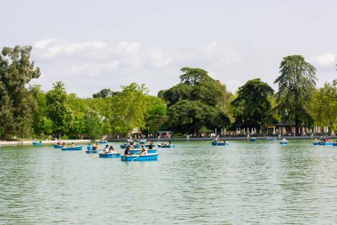Madrid, Spain. May 1, 2022. Children swimming in red kayaks, canoe on Retiro Park's blue pond in summer day. Active sports activities on the water. Kids in a camp have fun outdoors. Sport activities.