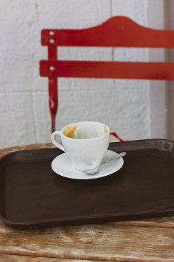 Bir fincan tabağında beyaz bir kahve fincanı bir kafedeki ahşap bir masanın üzerinde duruyor, kentsel bir çevrede bir kahve dükkanı. Sıcak bir içecek ile kavramsal dikey fotoğraf. Kırmızı sandalye.