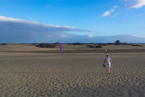 Woman in dress walking in the sand of desert dunes with steps in the desert sand, young woman walking in white sand on a bright summer day, holiday vacation concept