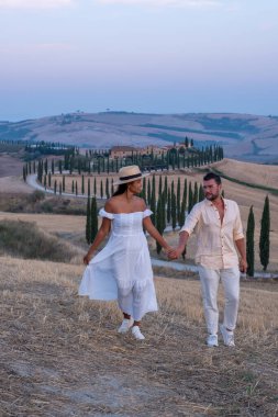 Tuscany manzarası, tahıl tarlaları, selvi ağaçları ve gün batımında tepelerde evler. Tuscany, İtalya, Avrupa, İtalya, Tarım Bakolenosu 'nda kıvrımlı yolu olan yaz kırsal arazisi 