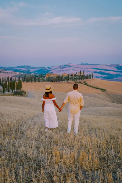 日没の丘の上に穀物畑、ヒノキの木や家を持つトスカーナの風景。トスカーナ、イタリア、ヨーロッパ、イタリア、アグリツーリズモBawrienoで湾曲した道路と夏の田園風景 — ストック写真