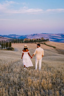 Tuscany manzarası, tahıl tarlaları, selvi ağaçları ve gün batımında tepelerde evler. Tuscany, İtalya, Avrupa, İtalya, Tarım Bakolenosu 'nda kıvrımlı yolu olan yaz kırsal arazisi 