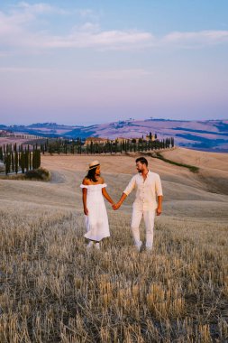 Tuscany manzarası, tahıl tarlaları, selvi ağaçları ve gün batımında tepelerde evler. Tuscany, İtalya, Avrupa, İtalya, Tarım Bakolenosu 'nda kıvrımlı yolu olan yaz kırsal arazisi 