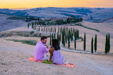 Tuscany manzarası, tahıl tarlaları, selvi ağaçları ve gün batımında tepelerde evler. Tuscany, İtalya, Avrupa, İtalya, Tarım Bakolenosu 'nda kıvrımlı yolu olan yaz kırsal arazisi 