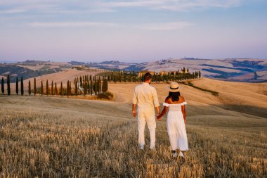 Tuscany manzarası, tahıl tarlaları, selvi ağaçları ve gün batımında tepelerde evler. Tuscany, İtalya, Avrupa, İtalya, Tarım Bakolenosu 'nda kıvrımlı yolu olan yaz kırsal arazisi 