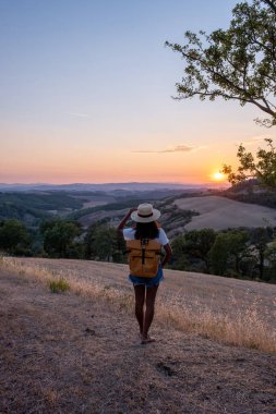Tuscany manzarası, tahıl tarlaları, selvi ağaçları ve gün batımında tepelerde evler. Tuscany, İtalya, Avrupa, İtalya, Tarım Bakolenosu 'nda kıvrımlı yolu olan yaz kırsal arazisi 