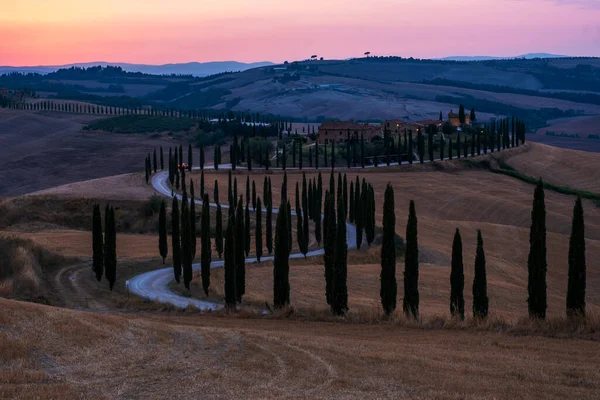 Paisaje toscano con campos de grano, cipreses y casas en las colinas al atardecer. Paisaje rural de verano con carretera curva en Toscana, Italia, Europa, Italia, Agriturismo Baccoleno —  Fotos de Stock