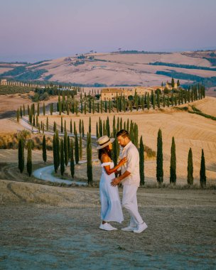 Toskana, Girit Senesi kırsal günbatımı manzarası. Köy çiftliği, selvi ağaçları, yeşil alan, güneş ışığı ve bulut. İtalya, Avrupa ve Tuscany, İtalya ve Avrupa 'da kıvrımlı yolu olan yaz kırsal arazisi