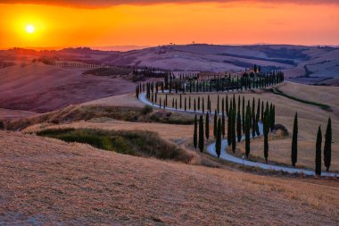Toskana, Girit Senesi kırsal günbatımı manzarası. Köy çiftliği, selvi ağaçları, yeşil alan, güneş ışığı ve bulut. İtalya, Avrupa ve Tuscany, İtalya ve Avrupa 'da kıvrımlı yolu olan yaz kırsal arazisi