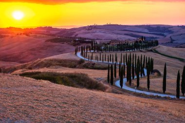 Toskana, Girit Senesi kırsal günbatımı manzarası. Köy çiftliği, selvi ağaçları, yeşil alan, güneş ışığı ve bulut. İtalya, Avrupa ve Tuscany, İtalya ve Avrupa 'da kıvrımlı yolu olan yaz kırsal arazisi