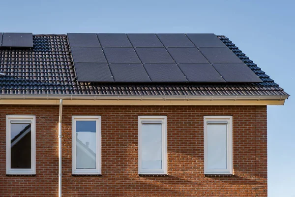 Нові будинки з сонячними панелями, прикріпленими на даху до сонячного неба, закриті новими будівлями з чорними сонячними панелями. Zonnepanelen, Zonne energie, Translation: Solar panel, Sun Energy — стокове фото