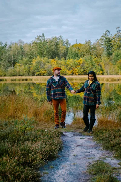 Para mężczyzna i kobieta w średnim wieku spaceruje w lesie jesienią w przyrodzie trekking z pomarańczowo-czerwonymi drzewami w sezonie jesiennym w Holandii Drentsche Aa — Zdjęcie stockowe