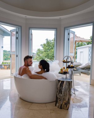 Lüks tatil beldesinde tatilde olan orta yaşlı bir çift küvette oturmuş okyanus manzaralı Avrupalı bir adam ve Asyalı bir kadın küvette oturuyor.