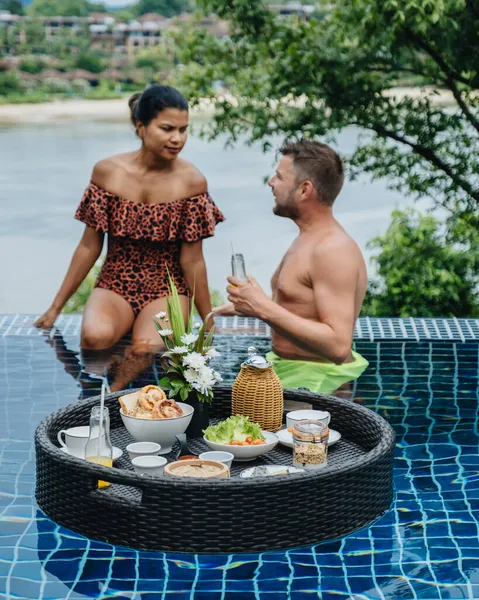 Couple homme et femme ayant plateau de petit déjeuner flottant dans un hôtel de luxe piscine, jeune femme avec chapeau profiter en station tropicale. Détente, Exotique voyage d'été, vacances, vacances et week-end — Photo