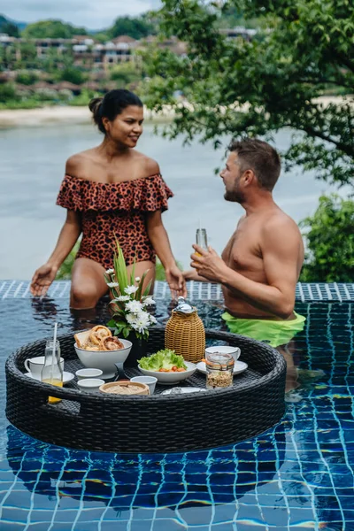 Couple homme et femme ayant plateau de petit déjeuner flottant dans un hôtel de luxe piscine, jeune femme avec chapeau profiter en station tropicale. Détente, Exotique voyage d'été, vacances, vacances et week-end — Photo