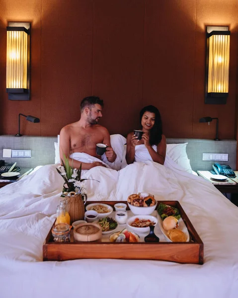 Paar ontbijten op bed, Europese man en Aziatische vrouw in bed met ontbijt in de ochtend — Stockfoto