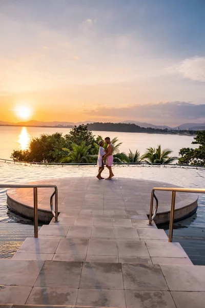 Par man och kvinna i medelåldern i poolen på en lyxig semester i Thailand, män och asiatisk kvinna i poolen ser ut över bukten titta på solnedgången — Stockfoto