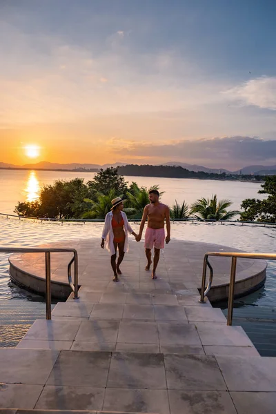 Couple homme et femme d'âge moyen dans la piscine sur des vacances de luxe en Thaïlande, les hommes et la femme asiatique dans la piscine donnant sur la baie en regardant coucher de soleil — Photo