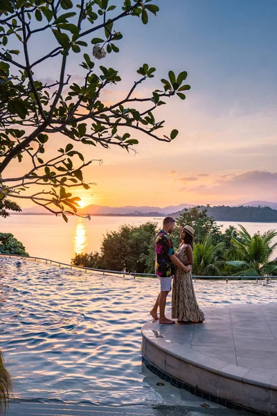 Couple man and woman mid age in swimming pool on a luxury vacation in Thailand, men and Asian woman in pool looking out over the bay watching sunset — Stock Photo, Image